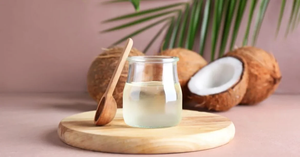 The Coconut Oil Debate: Can You Use Coconut Oil as Lube? A jar of coconut oil against a pink background on a wooden turntable with coconuts behind the jar. This is the image for can you use coconut oil as lube.