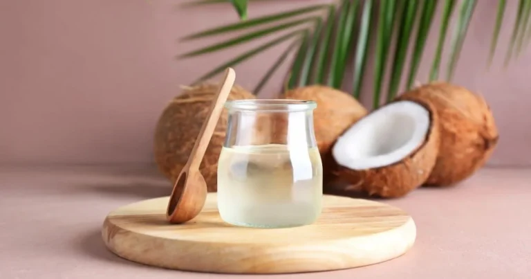 A jar of coconut oil against a pink background on a wooden turntable with coconuts behind the jar. This is the image for can you use coconut oil as lube.