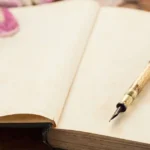 A Dominant's journal sitting on a desk with an antique pen on top of it. The journal is filled with journal prompts for Dominants.