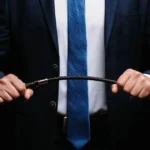 A dominant man holding a riding crop and wearing a suit. He is reading insightful quotes about dominance.