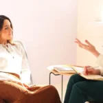 A sex coach working with a client on discussing sex and relationship coaching practices, the differences between sex coaching and sex therapy, and what to expect when hiring a sex coach.