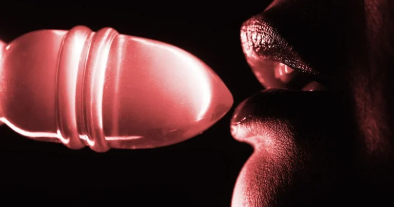 An image of a sex positive woman putting a sex toy to her lips seductively.