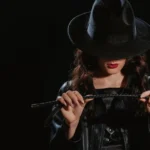 A Dom engaging in self-care while wearing a hat, red lipstick , and holding a crop. Self-care for Dominants allows her to be fully present in her dynamic.