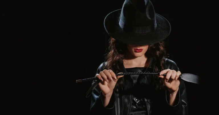 A Dom engaging in self-care while wearing a hat, red lipstick , and holding a crop. Self-care for Dominants allows her to be fully present in her dynamic.