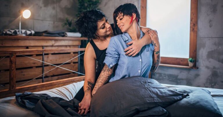 Lesbian couple cuddling in bed, illustrating neurodivergent BDSM aftercare with comforting physical closeness.